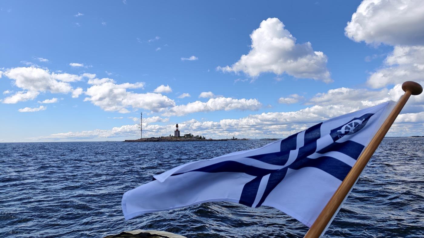 The Finnish ensign flying astern, a lighthouse on the horizon